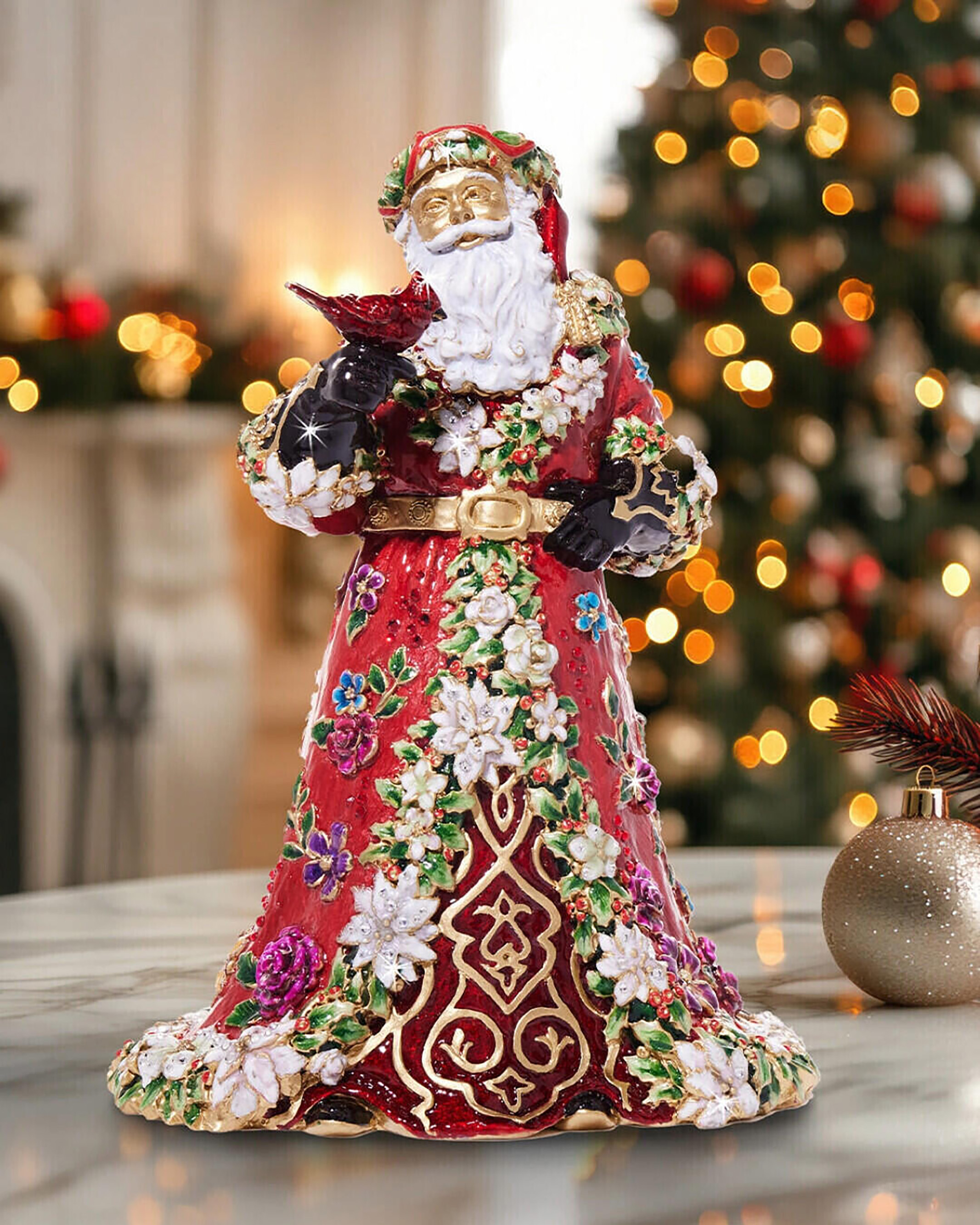 This figurine features intricate details, including a red robe adorned with white poinsettias and jewel-toned floral embellishments, accented with 14k gold. 