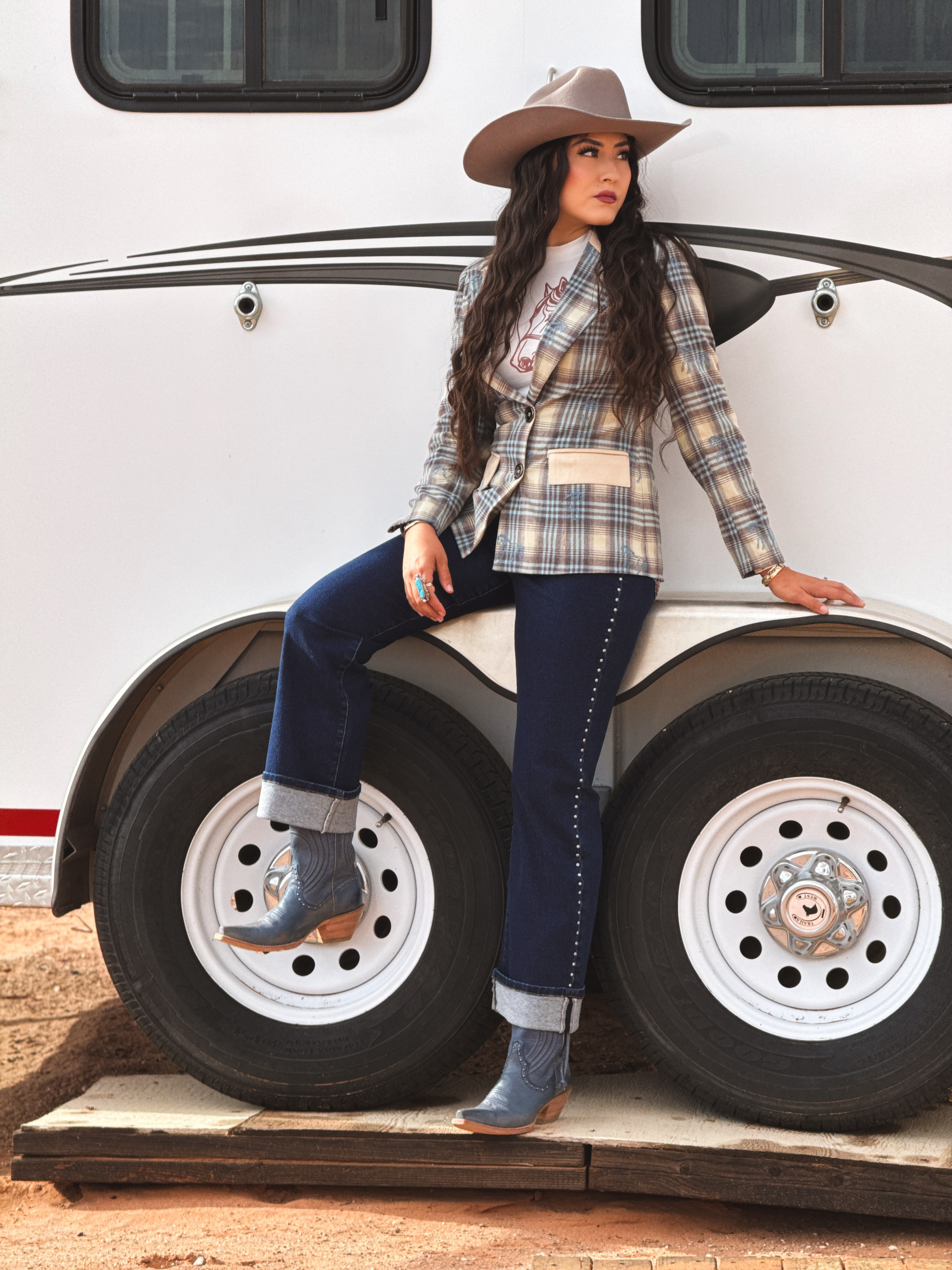 Plaid Western blazer with contrast pockets, graphic tee, studded dark denim jeans, cowboy hat, and boots for a polished rodeo, ranch, or boutique cowgirl look.