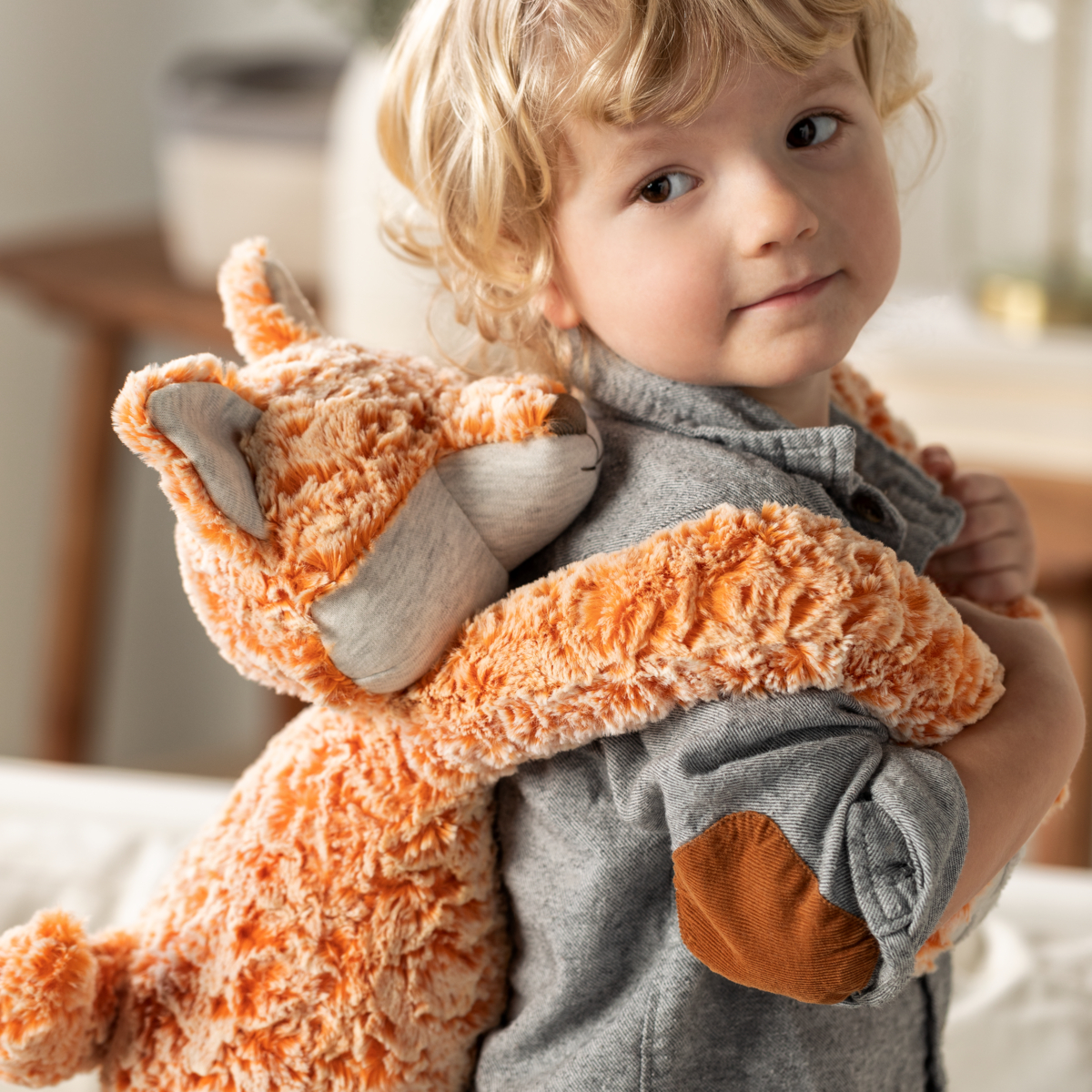 A cropped close up image of a young boy holding a weighted stuffed orange and white fox over his shoulders.