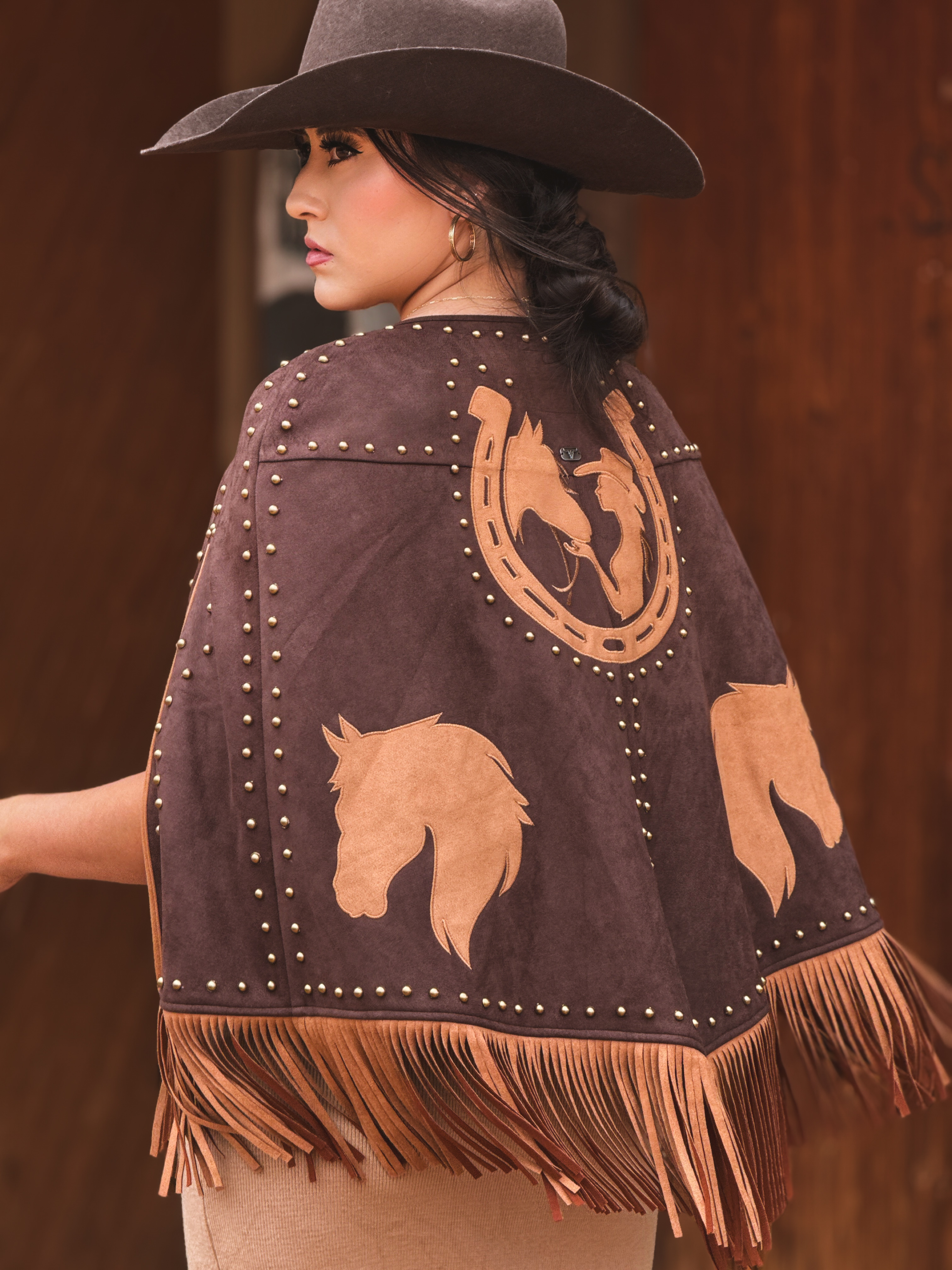 Western suede-style cape with horse appliqués, gold stud accents, and long fringe trim. A bold cowgirl statement layer perfect for rodeo looks, concerts, festivals, and western-chic styling.