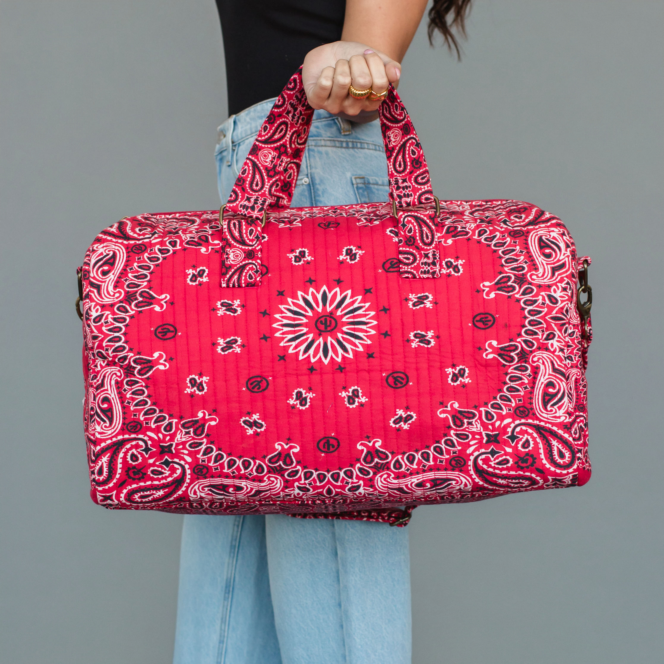 A red bandana patterned duffel bag featuring a classic paisley print, designed with sturdy top handles and an adjustable shoulder strap for easy carrying. Spacious interior is perfect for travel.