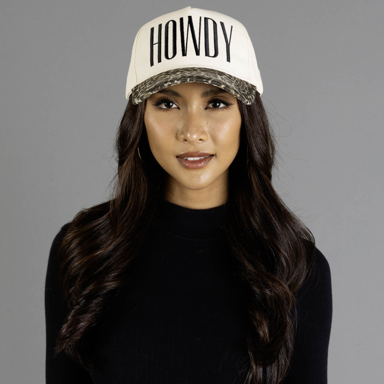 Ivory and leopard two-toned trucker hat featuring embroidered "HOWDY" text on the front, designed with a leopard print brim, classic structured fit, breathable mesh back, and adjustable snapback closu