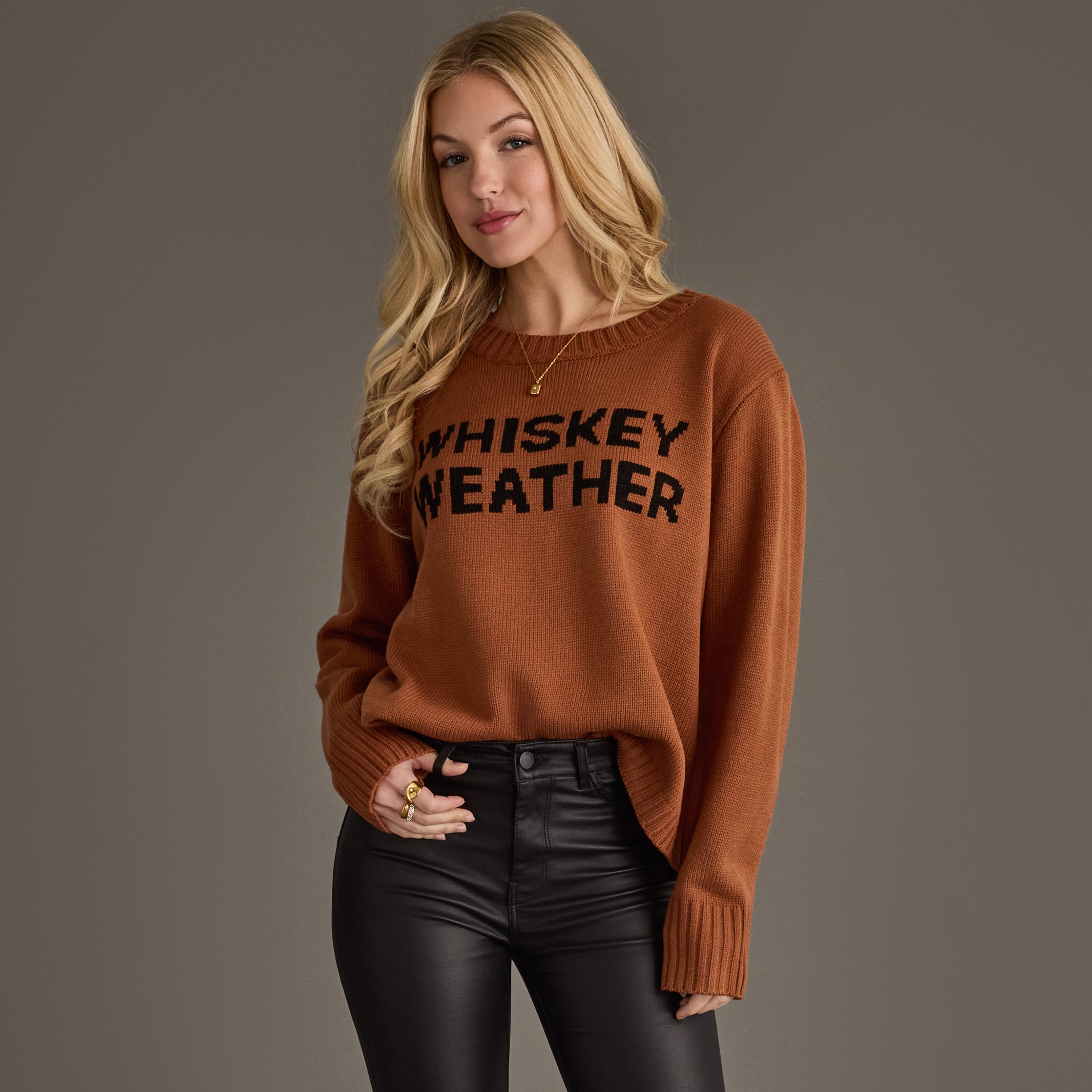 The Brown Whiskey Weather Sweater features a classic crew neckline, long sleeves with ribbed cuffs, and a cozy relaxed fit that's perfect for fall layering and seasonal styling.