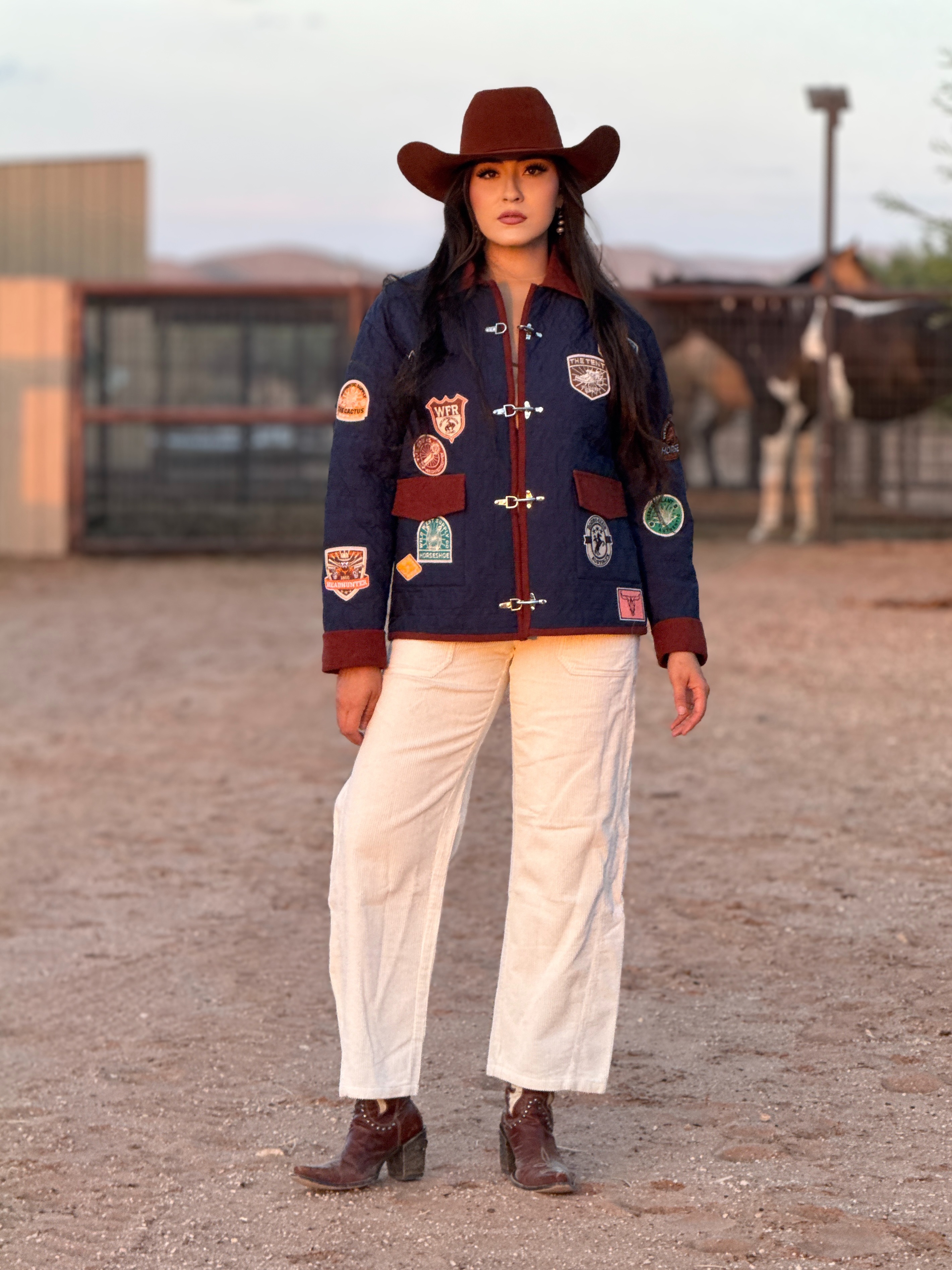 Navy Western patch jacket with burgundy trim, toggle closures, wide-leg cream pants, cowboy hat, and boots for a bold rodeo, ranch, or boutique cowgirl look.