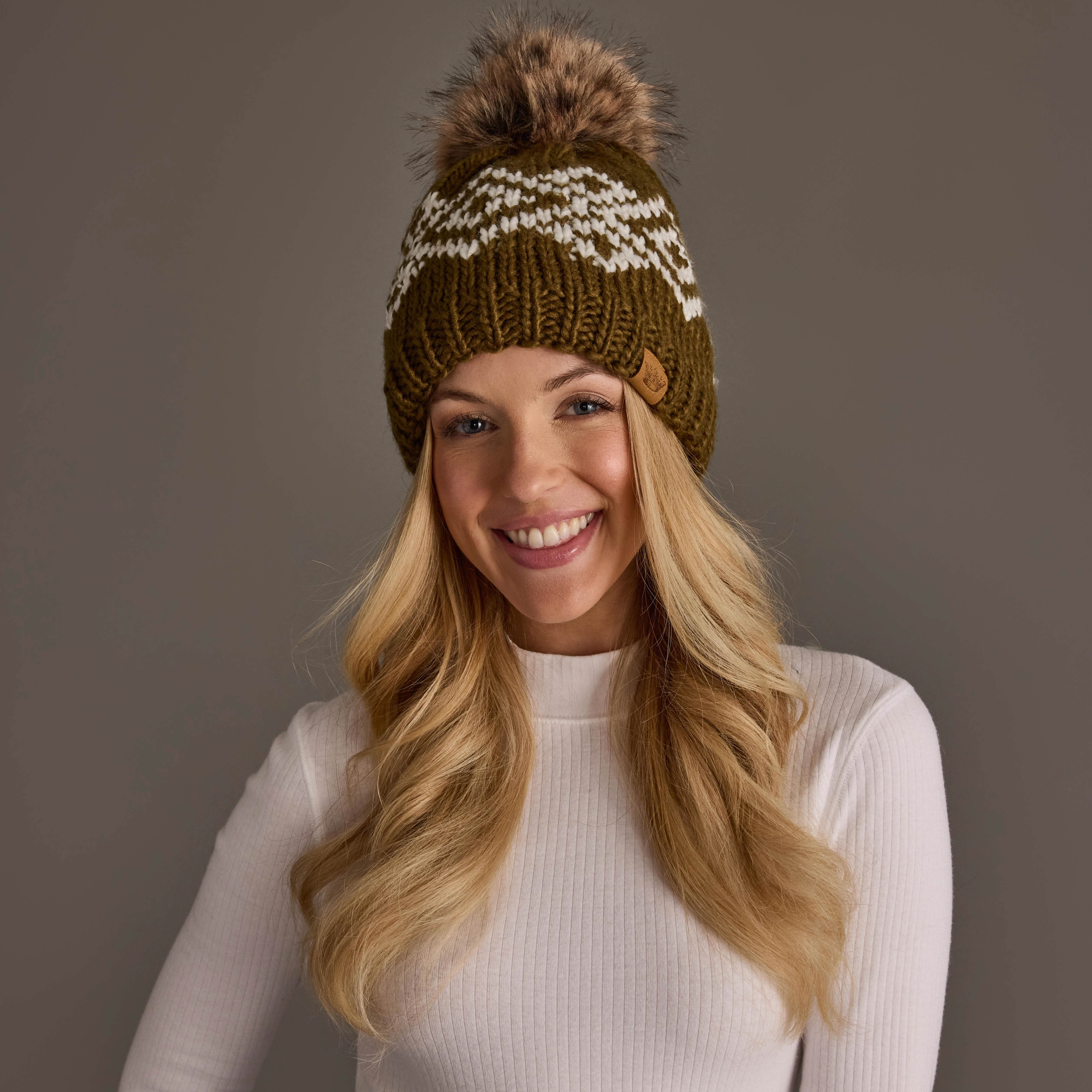 Camel and white patterned knit pom hat featuring a classic geometric knit design with contrasting white detailing, designed with a folded ribbed cuff and a natural faux fur pom on top for added warmth