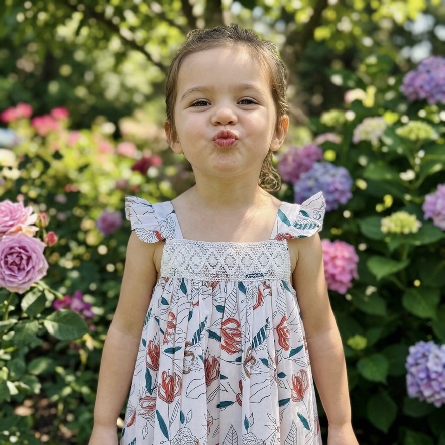 Soft cotton girls’ dress with coral floral block print, crochet lace and flutter sleeves. Lightweight, breathable and handcrafted with natural dyes—perfect for everyday wear.